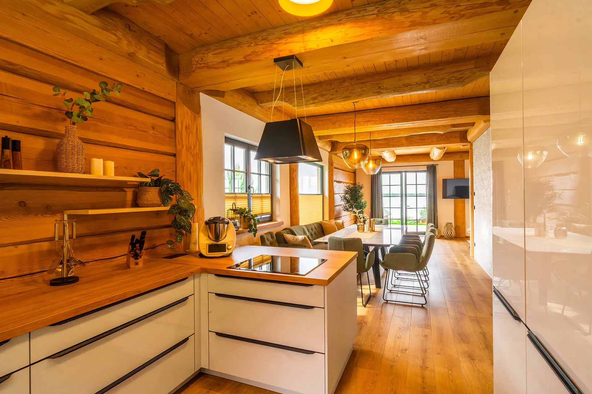 Offene Wohnküche im Ferienhaus mit Altholzdecke, Kochinsel und Blick über den Esstisch zum Gröberner See